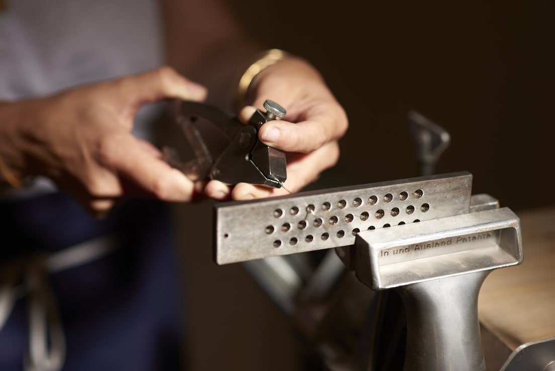 On voit les mains de la créatrice de bijoux Louise Vurpas en train de tirer un fil d'argent à travers une filière. Bijouterie-joaillerie sur-mesure